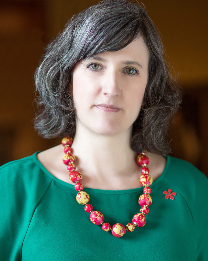 Headshot of Ainsley Cameron, looking directly into the camera. She is wearing a green shirt and a brightly colored necklace.